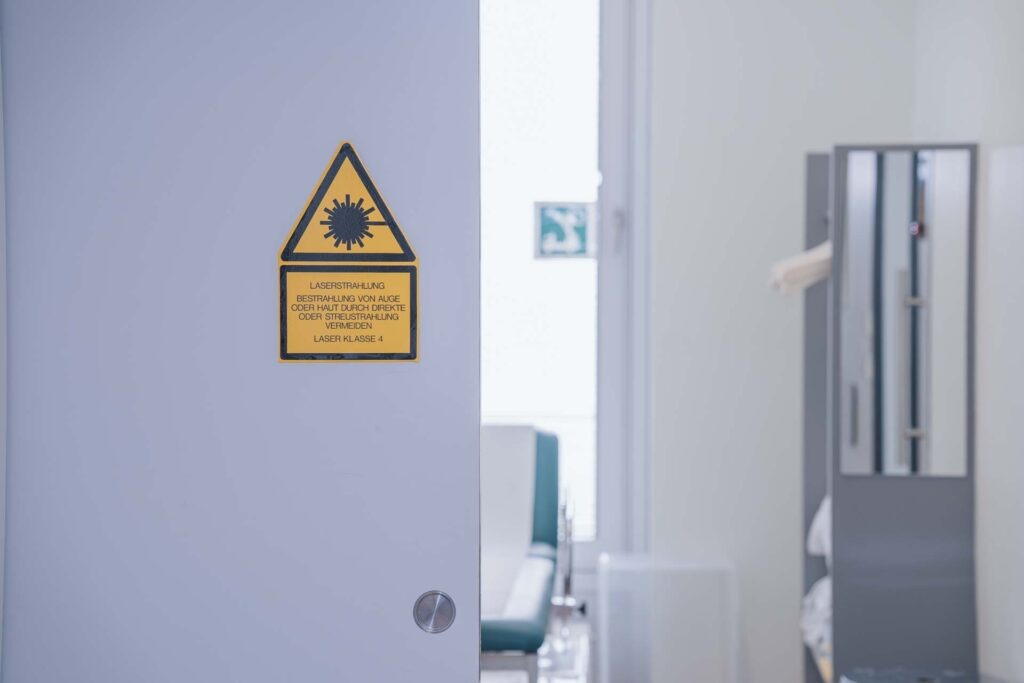 Blick in ein Behandlungszimmer, an der Tür ist ein Warnhinweis für Laserstrahlung