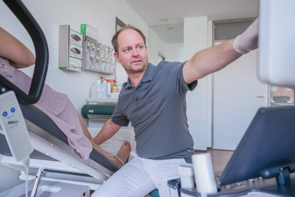 Dr. Claus Urbahn mit Ultraschallgerät am Patienten zeigt etwas auf dem Monitor